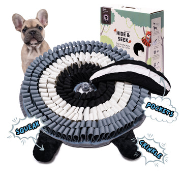 Black and gray skunk Hide and Seek snuffle mat with treat pockets squeaker legs and packaging beside small dog